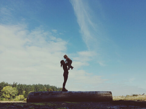 young mom playing with child on log out side in nature - big blue sky