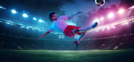 Kicking ball in high jump. Football or soccer player on full stadium and flashlights background....