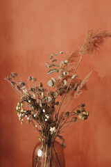 Beautiful autumn bouquet of dried flowers of brown shades in a glass vase on a red-orange vintage background