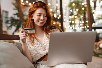 Image of ginger girl holding credit card and working with laptop