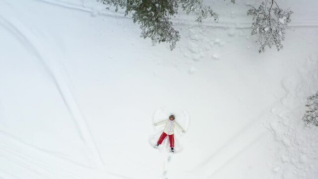 AERIAL. A young girl lying in the snow is painting an angel. The camera pans around and zooms in on her. Christmas Holidays.
