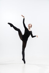 Fototapeta premium Weightless. Young and graceful ballet dancer in minimal black style isolated on white studio background. Art, motion, action, flexibility, inspiration concept. Flexible caucasian ballet dancer.