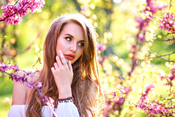 Close up portrait of amazing magazine tender woman with natural long hairs and perfect skin posing at blooming garden, spring time.
