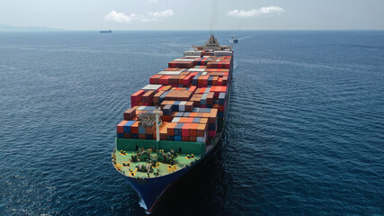 Fototapeta premium Aerial drone photo of huge container cargo Ship carrying load in truck-size colourful containers cruising deep blue open ocean sea 