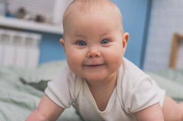 A child with big blue eyes lies on his tummy with an interested look