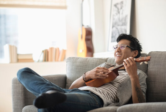 Man sitting on sofa and playing ukulele
