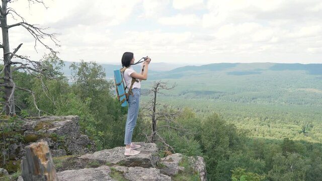 Happy young woman takes photos of nature on top of a mountain with her camera.