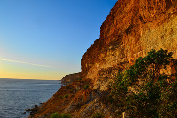 High red yellow sandy long cliffs of Fiolent with green bushes on the Black Sea coast in the light of sunset. Blue water and sky. Gradient on horizon. South Crimea