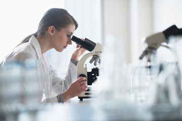 Female lab technician analyzing sample through microscope