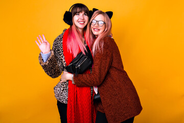 Spring lifestyle fashion portrait of two happy woman smiling and hugging, best friends posing, wearing fur trendy coats scarfs and funny ears.