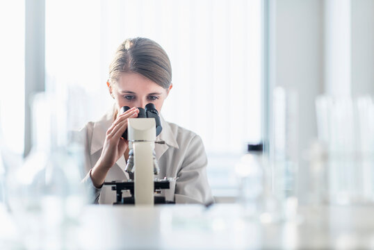 Female lab technician analyzing sample through microscope