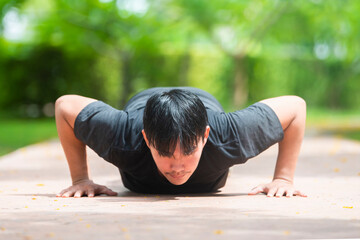 Fototapeta na wymiar Strength and motivation. Side view of young asian handsome man in sportswear doing push-up at park.