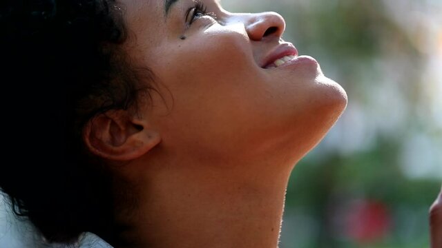 African woman worshiping outside, looking up to sky with faith