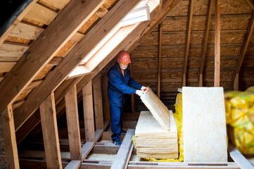 Naklejka na ściany i meble Roof insulation. A worker puts glass wool insulation in the attic.