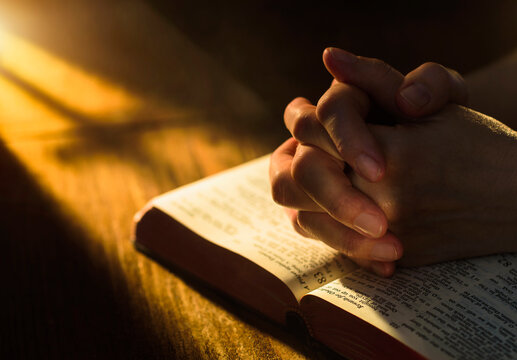 Close up of hands clasped on open Bible