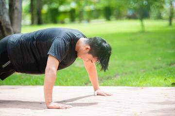 Fototapeta na wymiar Young asian man push ups on walking road in a park at morning. Copy space