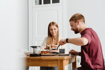 Image of joyful couple drinking coffee with pie while sitting at table