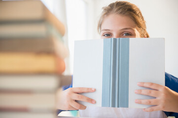 Teenage girl (12-13) hiding face behind book