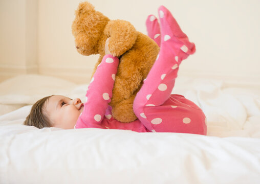 Naklejki Girl (2-3) lying on bed with teddy bear