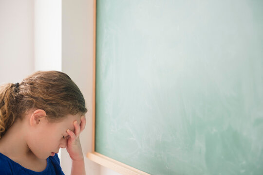 Girl doing face palm in front of green blackboard