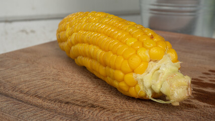 Delicious corn on the cob that's just been boiled is laying on a wooden board.
The brightly glowing yellow kernels form a recognizable pattern. The cob was seasoned with salt and hot spices.
