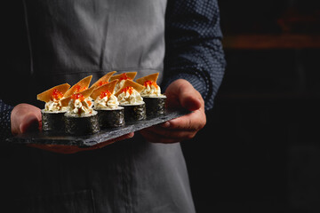 Sushi roll maki futo japanese food on a black stone plate in the hands of a waiter. Close up