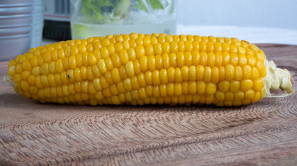 Delicious corn on the cob that's just been boiled is laying on a wooden board.
The brightly glowing yellow kernels form a recognizable pattern. The cob was seasoned with salt and hot spices.
