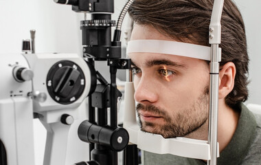 Handsome man getting an eye exam at ophthalmology clinic. Checking retina of a male eye close-up - obrazy, fototapety, plakaty