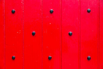 Close up of a vivid red wooden old door with black metal dots and vertical marks.
