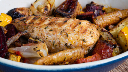 A grilled chicken is sitting in a ceramic plate alongside various root vegetables. The marks from the iron skillet is clearly visible as charred lines on the breast.
