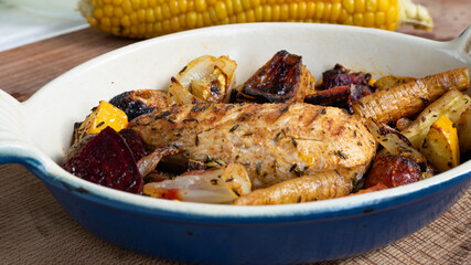 A grilled chicken is sitting in a ceramic plate alongside various root vegetables. The marks from the iron skillet is clearly visible as charred lines on the breast.
