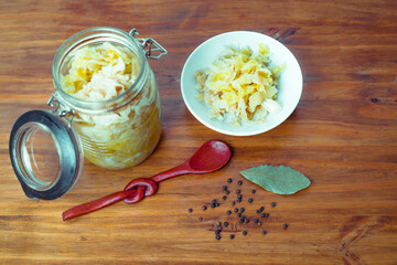 Jar of tasty sauerkraut on wooden table with peppermint and bay leaf, wooden spoon