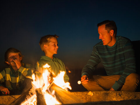 Man talking with his sons (10-11, 14-15) by campfire