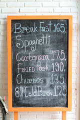Naklejka premium Handwritten menu on chalkboard in front of white brick wall.