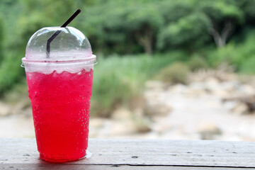 Iced red soda in a plastic cup on wooden table.