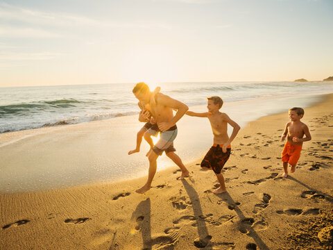 Father playing football on beach with his three sons (6-7, 10-11, 14-15)