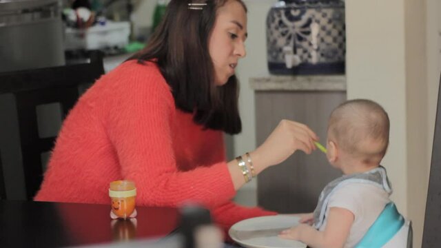 Madre mexicana joven da de comer a su hijo bebe en casa papilla