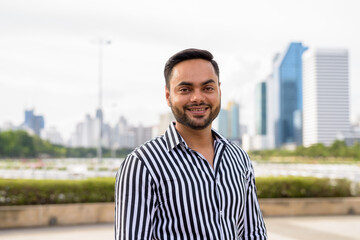 Young bearded Indian businessman relaxing at the park in the cit