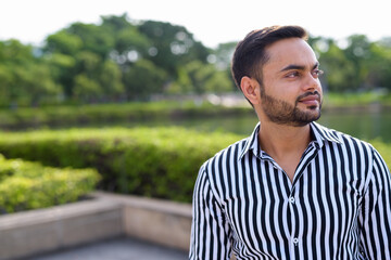 Fototapeta premium Young bearded Indian businessman relaxing at the park in the cit