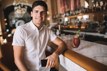 Smiling man sitting at counter with cocktail