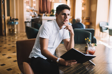 Pensive young man thinking over notes in cafe