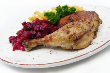Roasted chicken quarter leg with crispy golden brown skin, baked potatoes and beet salad on white plate. Food background.