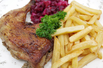 Roasted chicken quarter leg with crispy golden brown skin, baked potatoes and beet salad on white plate. Food background.
