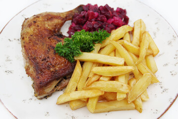 Roasted chicken quarter leg with crispy golden brown skin, baked potatoes and beet salad on white plate. Food background.