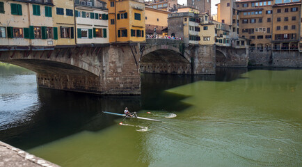 Fototapeta na wymiar Florence, Italy: Ponte Vecchio over the Arno river on a sunny day; a rowing boat is going under the bridge