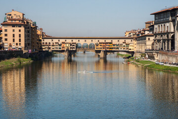 Fototapeta premium Florence, Italy: Ponte Vecchio over the Arno river on a sunny day; a rowing boat in front of the bridge