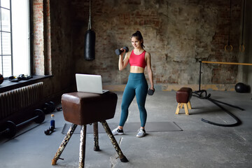 Sportswoman leads online fitness class.Woman stretching or yoga in gym using a laptop with online training. Regular sports boosts immune system and promote good health and resistance to diseases.