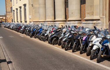 Florence, Italy: row of scooters parked along a road in front of  a classical building with pillars along the Arno river