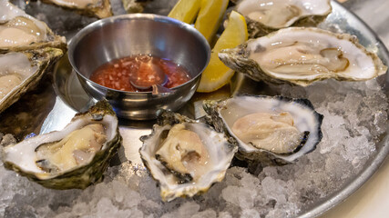 A platter of fresh organic raw oysters on ice with sauce and lemon at the restaurant.