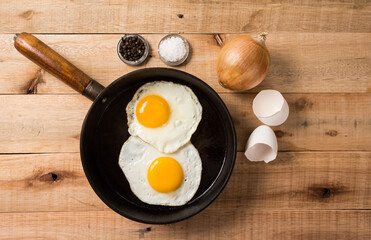fried eggs, in a frying pan, on wooden background. Top wiew.